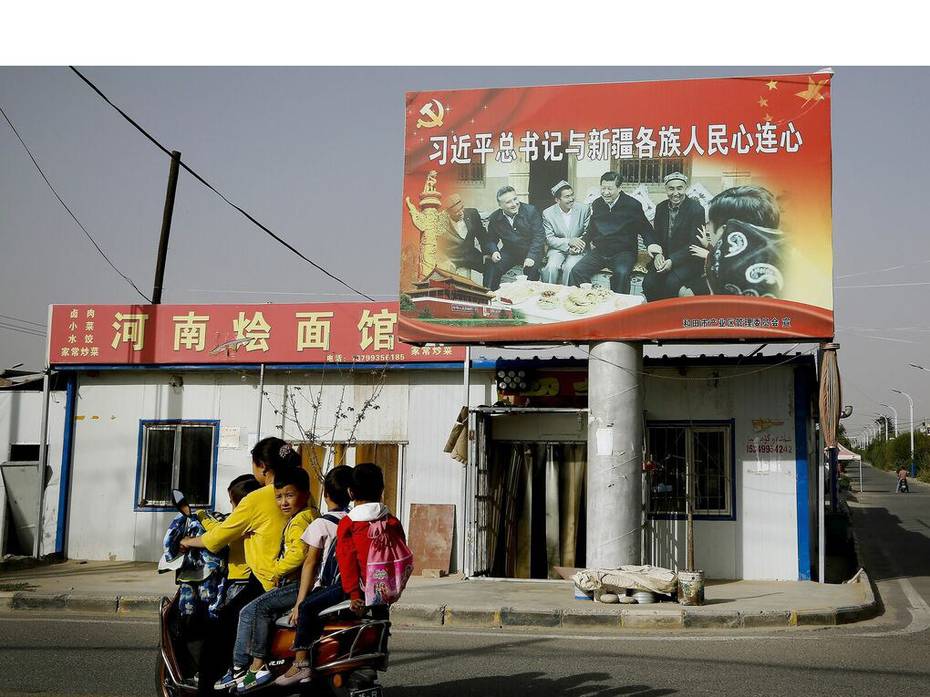 Frau mit drei Kindern auf einem Moped vor großen Propagandaplakaten der chinesischen Regierung