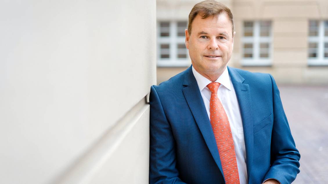 Christian Görke im Anzug lehnt an einer Hausecke des Parlamentsgebäudes